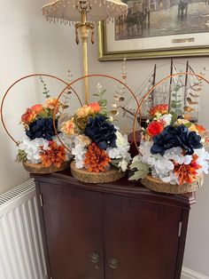 three baskets filled with flowers on top of a wooden cabinet next to a wall hanging