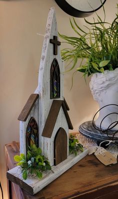 a small wooden church sitting on top of a table next to a potted plant