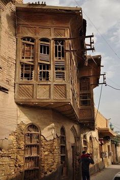 an old building with wooden balconies on the side and people walking down the street