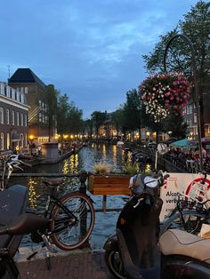 bicycles and scooters are parked along the water in front of buildings at dusk