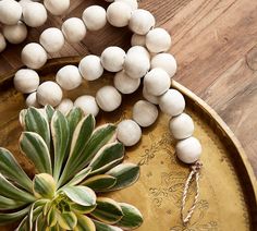 a wooden bead necklace with white beads and a green plant on a gold plate