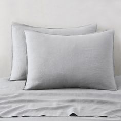 two light gray linen pillows sitting on top of a bed