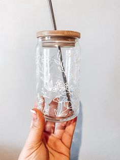 a hand holding a mason jar with a straw in it and flowers etched on the lid