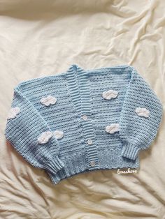 a blue knitted sweater with white clouds on the front and back, laying on a bed