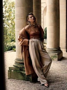 a woman is standing in front of some pillars with her hands on her hips and looking up at the sky