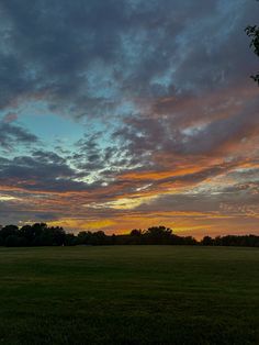 the sun is setting over an open field with trees in the foreground and clouds in the background