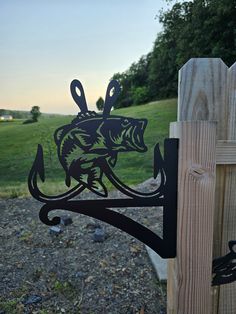 a metal fish on a wooden fence with grass and trees in the backgroud