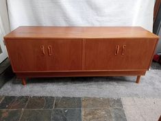 a wooden cabinet sitting on top of a stone floor next to a white sheet covered wall