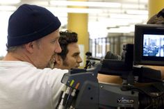 a man is filming another man in the background with a video camera on his shoulder