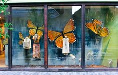 three glass windows with butterflies on them in front of a storefront window, and two mannequins dressed as women