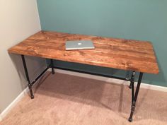 a wooden table with metal legs and a laptop on top, against a blue wall