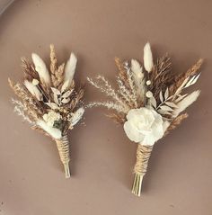 two boutonnieres with white flowers and feathers on a brown background, one is made out of dried grass