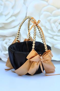 a black purse with gold beading and a large bow on the front, sitting in front of white flowers