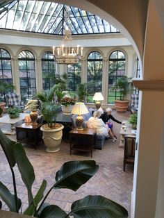 a living room filled with lots of furniture and plants inside of a glass walled building