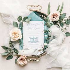 wedding stationery with roses and greenery on a white table cloth, surrounded by flowers