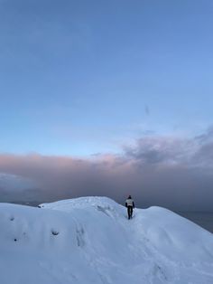 a man standing on top of a snow covered slope next to the ocean under a cloudy sky