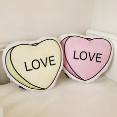 two heart shaped pillows sitting on top of a bed next to each other with the word love written on them