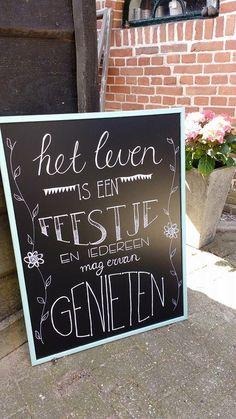 a chalkboard sign sitting on the sidewalk next to a brick wall and potted plant