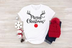 a white t - shirt with the words merry christmas on it next to a red hat