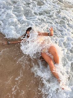 a woman laying on her stomach in the water at the edge of the beach,