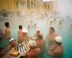 a group of men playing chess in a hot pool with steam coming from the water