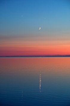 the moon is reflected in the calm water at sunset, with an orange and blue sky