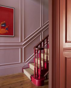 a staircase with pink walls and red railings next to a painting on the wall