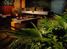 an outdoor kitchen is lit up at night with candles on the counter and potted plants