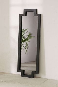 a black mirror sitting on top of a white wall next to a plant in a vase