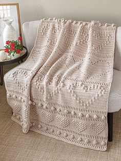 a crocheted blanket sitting on top of a chair next to a vase with flowers