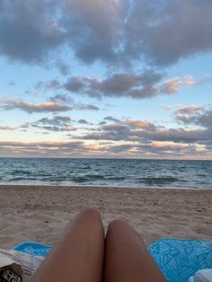 a woman laying on top of a blue towel next to the ocean under a cloudy sky