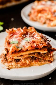 a stack of lasagna sitting on top of a white plate next to a slice of pizza