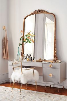 a white vanity with a mirror, stool and flowers on it in a room that is all white