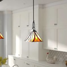 two stained glass lights hanging from the ceiling in a kitchen with white cabinets and counter tops