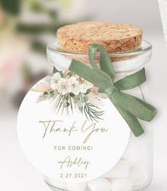 a glass jar filled with white chocolate covered marshmallows and a green bow