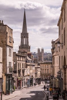 people are walking down the street in front of buildings and a church steeple is seen in the distance