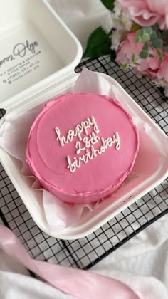 a pink birthday cake sitting on top of a white platter next to flowers and ribbon