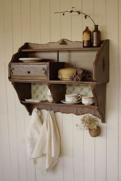 an old wooden shelf with dishes and cups on it next to a wall mounted towel rack