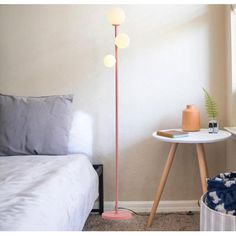 a pink floor lamp next to a bed in a room with white walls and carpet