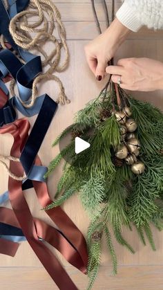 someone is making a christmas wreath out of pine cones and blue satin ribbons on a wooden table