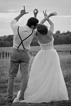 a bride and groom standing in the grass with their arms raised up to each other