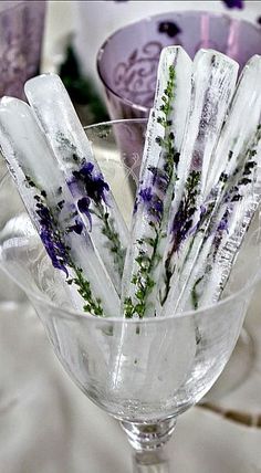 there are some ice sticks in the glass cup on the table with purple and white flowers