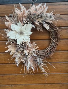 a wreath with white flowers and dried grass on a wooden surface, ready to be used as a decoration