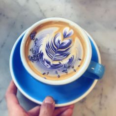 a person holding a blue and white cup filled with latte art on top of a saucer