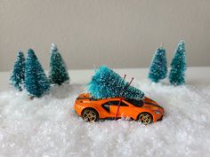 an orange toy car with a christmas tree on the roof in front of some small trees