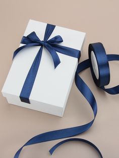 a white box with a blue ribbon and a roll of tape next to it on a table