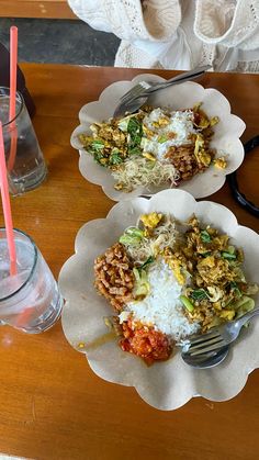 two plates of food on a table next to a glass of water and a plastic fork