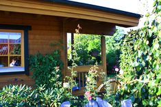 there is a small wooden house in the garden with flowers and plants growing around it