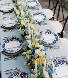 a long table is set with blue and white plates, silverware, and flowers