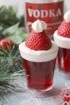 two cups filled with red liquid and topped with whipped cream, sitting next to a bottle of vodka